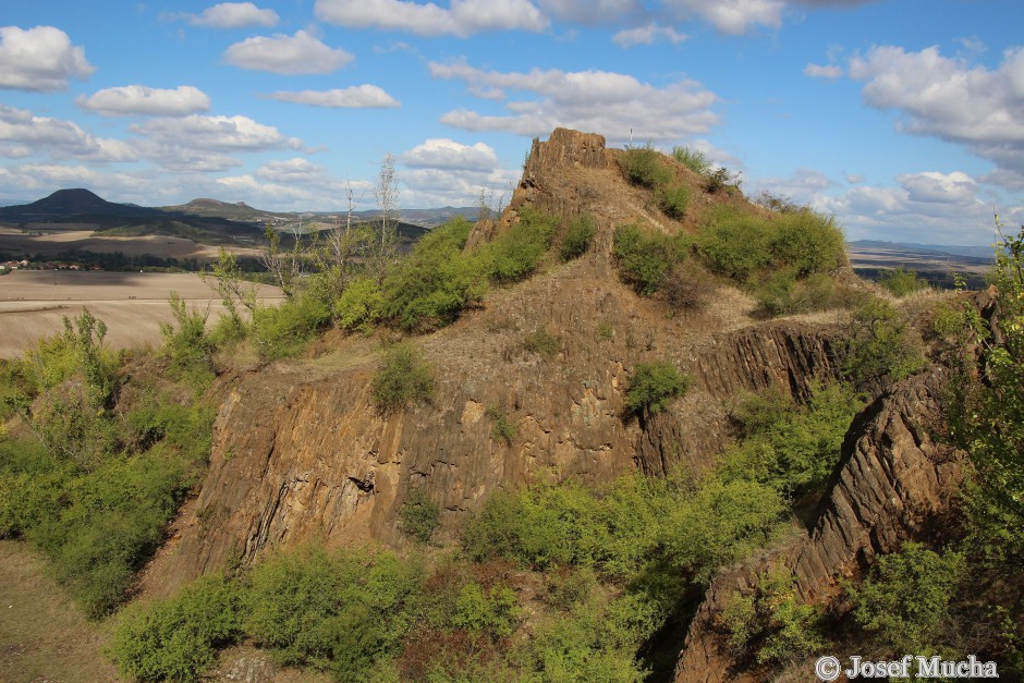Blšanský chlum - vrchol - sloupcová odlučnost bazaltu, přívodní dráha (diatréma) bývalého vulkánu, vlevo v pozadí vrch Oblík